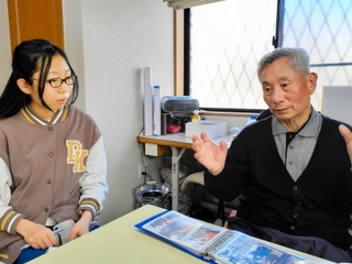 震災直後の写真を見せてもらい、崔敏夫さん（右）の話に耳を傾ける山崎まはなさん＝神戸市須磨区千歳町１