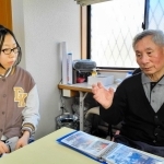 震災直後の写真を見せてもらい、崔敏夫さん（右）の話に耳を傾ける山崎まはなさん＝神戸市須磨区千歳町１