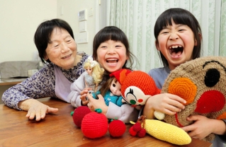 「まきちゃん」こと小林眞紀子さん（左）に作ってもらったぬいぐるみや、人形の洋服を抱きしめて、ご機嫌の三好莉帆さん（右）、華帆さん＝明石市太寺４