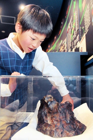 約１９０年前にアフリカで発見された隕石に触れる原壱之心さん。宇宙から飛んできた隕石のパワーを感じる＝明石市立天文科学館