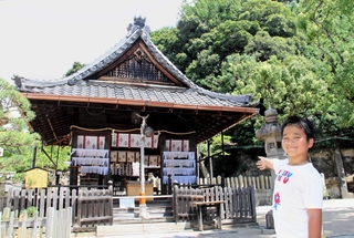 木々の緑を背にした拝殿を紹介する小林絃太さん＝神戸市兵庫区上祇園町、祇園神社
