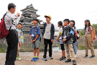 案内役の後藤芳孝さん（左）から国宝松本城の魅力を聞くこども記者ら＝長野県松本市