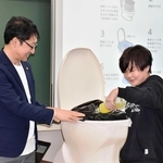 便器にセットした携帯トイレへ、色水を入れてためしてみる児童＝東京都大田区の区立出雲小学校