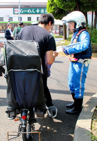 自転車利用者に注意をよびかけるチラシを配る警視庁の警察官＝東京都葛飾区