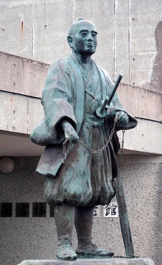 測量用のくさりを持って立つ間宮林蔵の銅像＝茨城県つくばみらい市の間宮林蔵記念館前