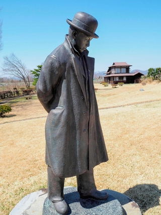 大正期の写真を再現した宮沢賢治の銅像。おくは賢治が住んだ家＝岩手県花巻市の県立花巻農業高校