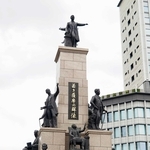 留学生ら１９人の銅像が並ぶ「若き薩摩の群像」。中央のいすにすわっている像が長沢鼎＝鹿児島市のＪＲ鹿児島中央駅前