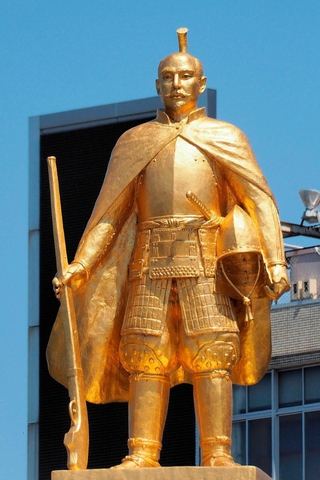 マントを羽織り、鉄砲とかぶとを持つ金色の織田信長像＝岐阜市のＪＲ岐阜駅前
