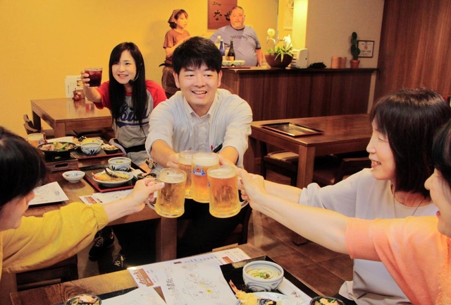 夜の商店街を楽しむ大人向けツアー「水道筋的裏ミシュラン」。参加者と乾杯する末吉佳希記者＝灘区水道筋２、うどん店「な也」