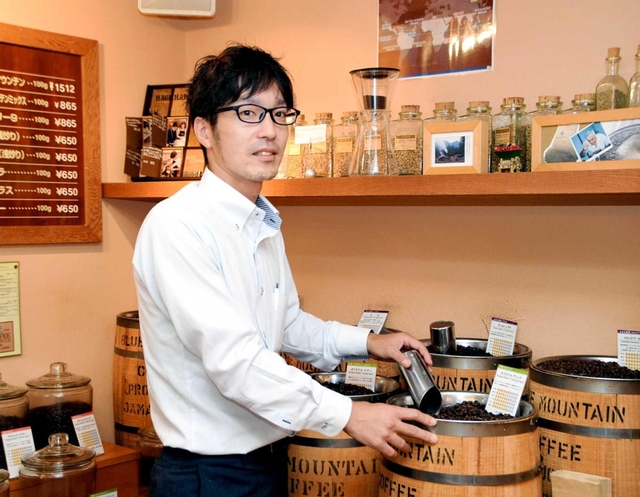 本社１階に設けられた直売店で、コーヒー豆をすくう萩原英治さん＝灘区城内通１