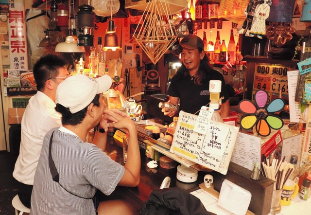 キャンプ道具の説明をお客さんにする殿本真一さん＝焼き鳥店「チンタ」