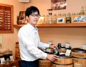 本社１階に設けられた直売店で、コーヒー豆をすくう萩原英治さん＝灘区城内通１