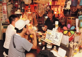 キャンプ道具の説明をお客さんにする殿本真一さん＝焼き鳥店「チンタ」
