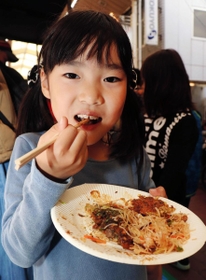 「長い列を待って良かった」とお好み焼きを頰張る宗和明花音ちゃん＝神戸市長田区腕塚町２