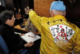 利用者に商品を手渡す萬福グージーサービス宅配の配達員（右）＝神戸市長田区内