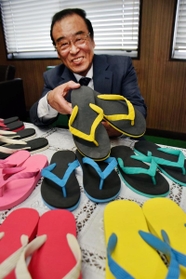 世界初のビーチサンダルを手にする内外ゴムＯＢ会会長の相川征四郎＝明石市