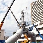 巨大なクレーンを使い、骨組みにパーツを取り付ける作業が進むモニュメント＝若松公園