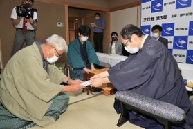 立会人の淡路仁茂九段（左）に封じ手が入った封筒を渡す木村一基王位（右）。中央は藤井聡太棋聖＝４日午後、神戸市北区有馬町、旅館「中の坊瑞苑」（撮影・斎藤雅志）