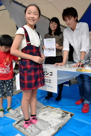 新聞紙のスリッパで、ガラス片に見立てた卵の殻を踏む子ども＝神戸ハーバーランド