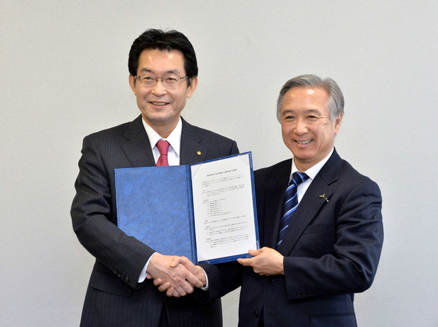 連携を結ぶ協定書を掲げ、握手を交わす関西学院大の村田治学長（右）と神戸新聞の高士薫社長＝神戸市中央区東川崎町１、神戸クリスタルタワー
