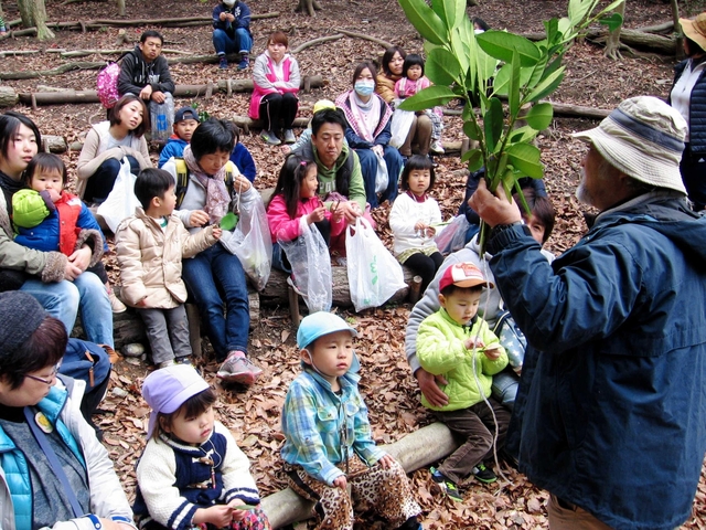 山崎春人さん（右）から山の自然を使った遊びについて教わる親子＝垂水区小束山手１