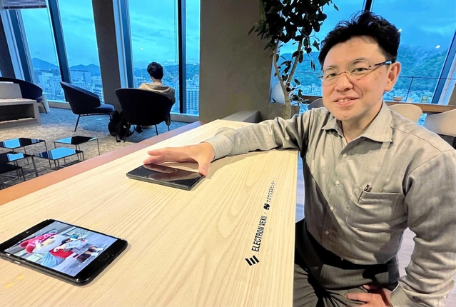 特許技術を搭載したスマートテーブルでスマホを充電する池内社長＝アンカー神戸