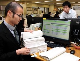 神戸市職員とレセプトチェックの効率化を検討するモンスター・ラボの平石真寛さん（奥）＝神戸市役所
