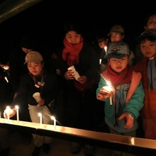 慰霊碑前の燭台に火をともす子どもら＝１７日午前５時５３分、神戸市東灘区本山北町３、本山第一小学校