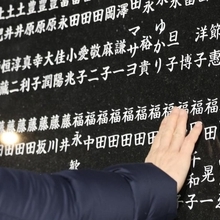 犠牲者の名前をそっとなでる女性＝１７日午前５時５４分、西宮市奥畑、西宮震災記念碑公園