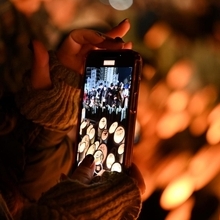 スマートフォンで竹灯ろうの明かりを撮影する参列者＝１７日午前６時９分、神戸市中央区加納町６、東遊園地（撮影・大田将之）