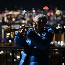 神戸の街を背に、トランペットの音色を響かせる松平晃さん＝１７日午前６時１４分、神戸市中央区、ビーナスブリッジ（撮影・風斗雅博）
