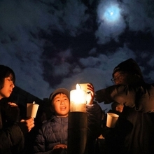 月が輝き、寒風吹き抜ける校庭で、ろうそくをともす追悼行事の参加者たち＝１７日午前５時３５分、神戸市東灘区本山北町３、本山第一小（撮影・三浦拓也）