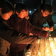 ろうそくに人をともす子どもたち＝１７日午前５時３６分、神戸市長田区若松町１０（撮影・中西大二）