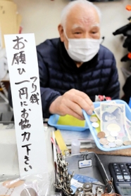 日々、大量の小銭を扱うという花崎治良さん。レジ前の立て札で協力を求める＝神戸市兵庫区東山町１