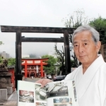 ８６年の役目を終えた鳥居を背に、阪神・淡路大震災の記録集を手にする六車勝昭宮司＝いずれも神戸市中央区下山手通１、生田神社