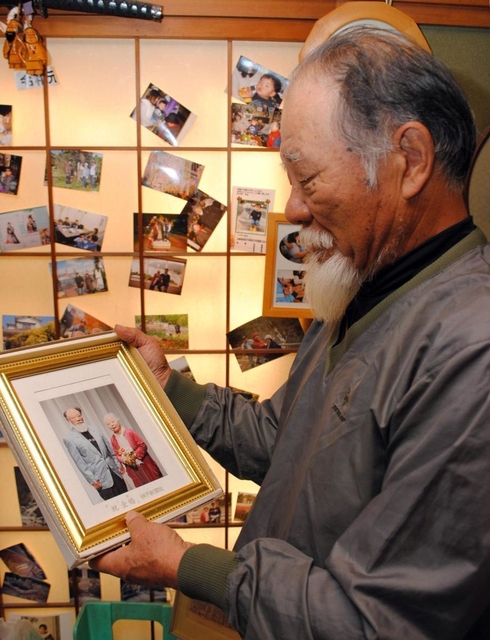 昨年出席した金婚式典の写真を見る高橋健二さん。認知症の妻としゑさんを支える＝加古川市内