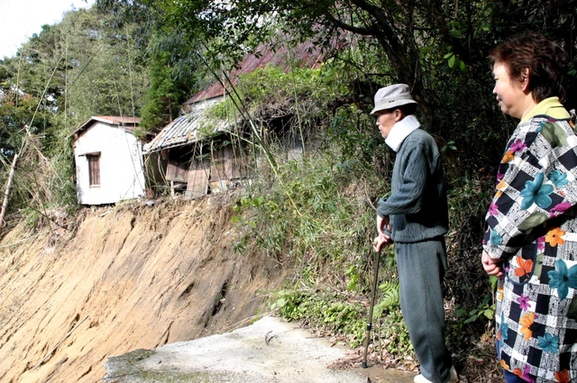 崩れた町道を見つめる山田さん夫妻。つめ跡は今も深い＝１１月１６日、兵庫県津名町興隆寺