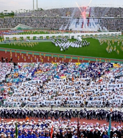写真上＝復興　式典前演技では大きな未来への架け橋が登場し、花火と歌声がフィナーレを飾った。写真下＝声援　県内のスポーツクラブの子どもたちが、全都道府県の選手団に「ガンバレ」のメッセージを掲げ、熱狂的に迎えた。いずれも神戸市須磨区、ユニバー記念競技場
