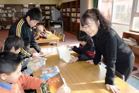 震災の本を読む児童と吉田さん（右）。「神戸で地震があったこと知ってる？」＝神戸市西区学園西町
