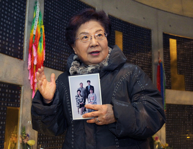 家族の写真を手に、基弘さんの銘板が掲げられたモニュメントを訪れた竸恵美子さん＝１６日午後、神戸市中央区加納町６（撮影・峰大二郎）