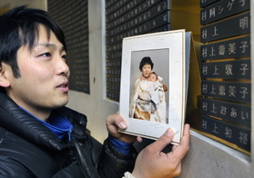 村上明さん、壽美子さんの銘板の前に立つ孫の健太さん。幼いころの写真を掲げ成長を報告した＝１７日午前７時８分、神戸市中央区加納町６、東遊園地（撮影・吉田敦史）