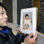 村上明さん、壽美子さんの銘板の前に立つ孫の健太さん。幼いころの写真を掲げ成長を報告した＝１７日午前７時８分、神戸市中央区加納町６、東遊園地（撮影・吉田敦史）