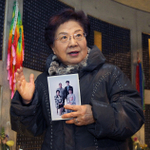 家族の写真を手に、基弘さんの銘板が掲げられたモニュメントを訪れた竸恵美子さん＝１６日午後、神戸市中央区加納町６（撮影・峰大二郎）
