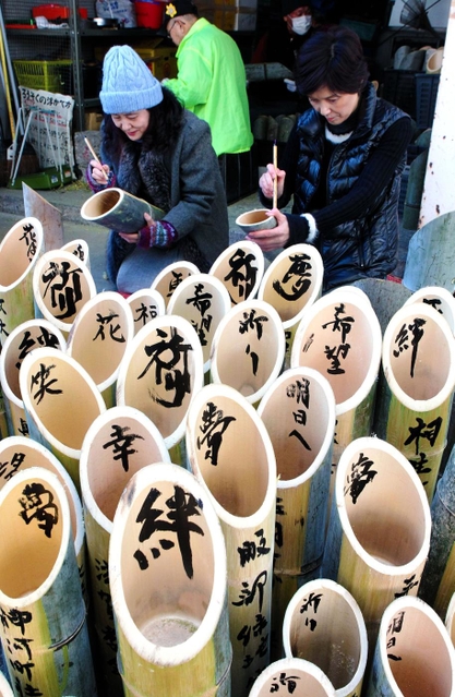 竹灯籠に文字を書き入れる参加者＝７日午前、神戸市灘区（撮影・吉田敦史）