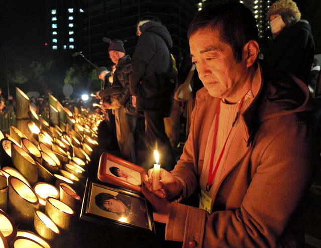 典子さんと康之さんの遺影を手に、竹灯籠を見つめる木皿俊克さん＝１７日午前５時３１分、神戸市中央区加納町６（撮影・宮路博志）