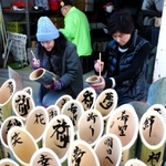 竹灯籠に文字を書き入れる参加者＝７日午前、神戸市灘区（撮影・吉田敦史）