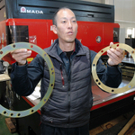 新社屋で鉄道用の機械部品を手にする高田社長＝神戸市西区見津が丘５