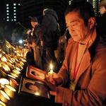 典子さんと康之さんの遺影を手に、竹灯籠を見つめる木皿俊克さん＝１７日午前５時３１分、神戸市中央区加納町６（撮影・宮路博志）