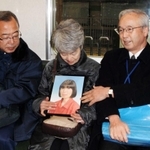黒田裕子さんの遺影を持ち、臨時便の出発を待つ宇都（うと）幸子さん（中央）、高橋守雄さん（右）ら＝１７日午前４時１２分、神戸市西区糀台５、市営地下鉄西神中央駅