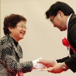 今年の竸基弘賞に輝いた研究者と握手する竸恵美子さん（左）＝神戸国際会議場